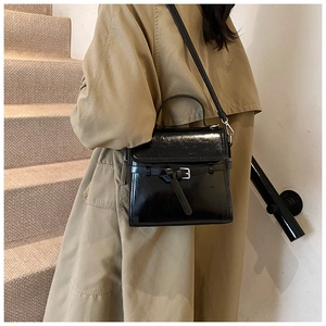 Details einer glänzenden schwarzen Lackledertasche mit Schnalle und Schultergurt