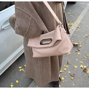 Detail of a dusty pink pleated shoulder bag with oval metal handle and textured finish