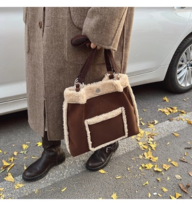 Detail of faux shearling trim on a brown suede tote bag held by a model outdoors