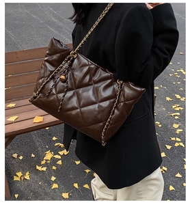 Detail of dark brown quilted PU tote bag with gold chain strap in autumn street setting