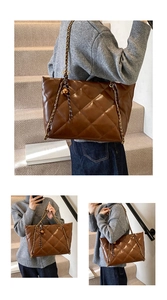 Detail of a brown quilted tote bag with chain strap and golden ball pendant charm