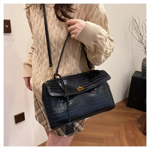 Close-up of black croc-embossed tote bag with golden twist-lock and slim shoulder strap
