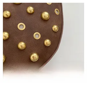 Détail d'un sac en cuir mat marron foncé avec des clous dorés radiaux et des œillets