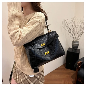 Detail of black crocodile-textured tote bag with gold hardware on minimalist model display
