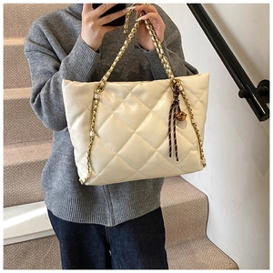 Detailed shot of white quilted tote bag featuring gold chain strap and bell pendant