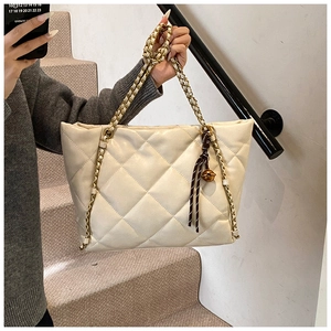 Close-up of cream quilted tote bag featuring gold chain strap and tassel bell charm