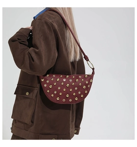 Détail du sac bandoulière demi-lune bordeaux avec rivets dorés et œillets métalliques