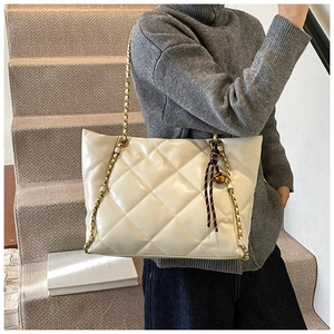 Close-up of quilted tote bag featuring gold chain strap and elegant tassel pendant
