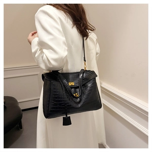 Detail of elegant black crocodile pattern tote bag shown worn with a white winter coat