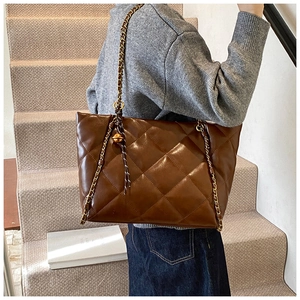 Detail of a brown quilted tote bag with gold chain strap and spherical metal ornament