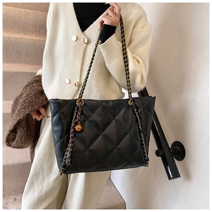 Detail of black quilted tote bag with gold chain strap and spherical pendant on a model