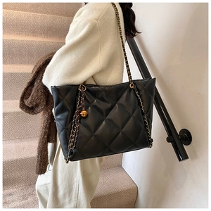 Detail view of black quilted tote bag with gold chain strap and metal ball ornament