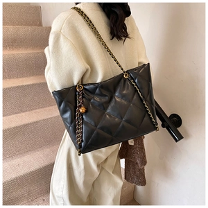 Detail of black quilted tote bag with gold chain strap and spherical metal pendant