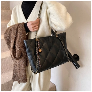 Close-up of black quilted PU leather tote bag with gold chain strap on model