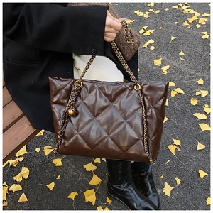 Detail of dark brown quilted leather tote bag with gold chain strap on park bench