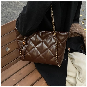 Detail of dark brown quilted tote bag with gold chain strap and decorative tassel