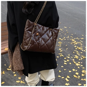 Detail of dark brown quilted tote bag with gold chain strap and decorative bell charm