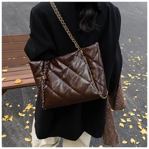 Detail of dark brown quilted tote bag with metal chain strap in an autumn setting