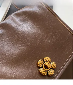 Detail of dark brown leather handbag featuring a gold floral twist lock with engravings