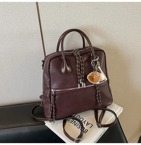 Dettaglio della borsa vintage bordeaux con tiri zip intrecciati e ciondolo da baseball