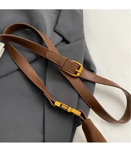 Detail eines verstellbaren braunen Lederriemens mit goldener Schnalle auf grauem Blazer