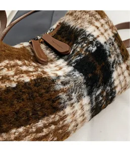 Detail von Plüsch-Tartan-Stoff mit braunen Leder-Doppelreißverschlüssen an Handtasche