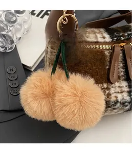 Detail eines flauschigen Kirsch-Anhängers mit grünen Lederblättern an einer Handtasche
