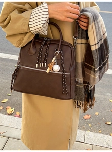 Dettaglio della cartella in pelle PU marrone scuro con ciondolo da baseball e zip a righe