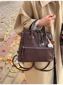 Zaino vintage in pelle marrone con ciondoli da baseball su foglie d'autunno