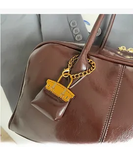 Detail of dark brown polished PU leather handbag with golden chain and logo pendant