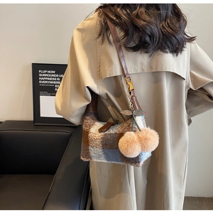 Detail of wool blend plaid crossbody bag with cherry fur ball charms on camel coat