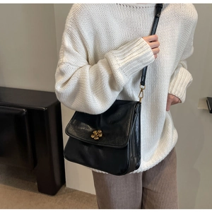 Close-up of black leather crossbody bag with gold flower buckle on white knit sweater