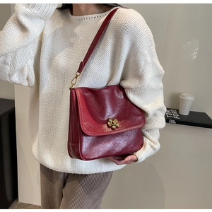 Detail of burgundy leather shoulder bag featuring a gold floral-shaped twist lock buckle