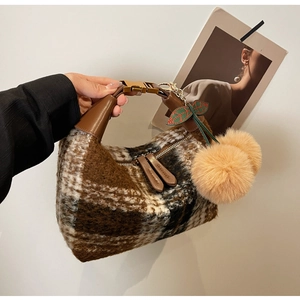 Detail of brown plaid plush handbag with leather handles and orange cherry pom-poms