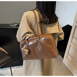 Detail of a brown glossy PU leather Boston bag featuring a gold padlock and dual handles