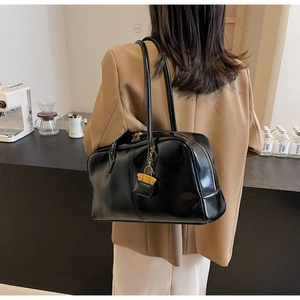 Detail of a large black PU leather underarm bag with zipper closure and mini bag charm