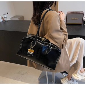 Detail of a large black glossy PU leather hobo bag with gold zippers worn on shoulder