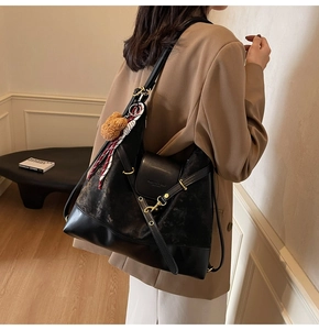Detail of large black matte tote bag featuring gold hardware and plush bear charm