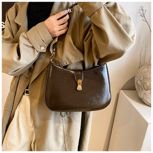 Detail of dark brown semi-moon leather shoulder bag with gold metal buckle on beige coat