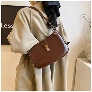 Detail of dark brown glossy leather underarm bag with gold metal clasp on model
