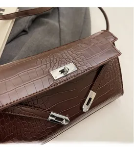Close-up of silver metal twist lock and crocodile texture on dark brown shoulder bag