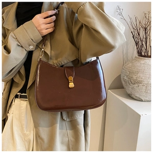 Detail of dark brown semi-circle bag with glossy finish and gold trapezoid metal clasp