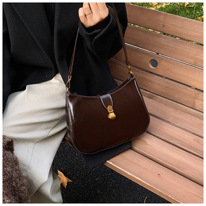 Detail of glossy coffee brown leather shoulder bag with gold buckle on wooden bench
