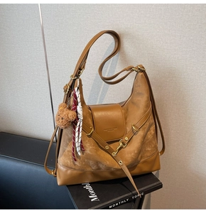 Detail of brown tote bag with leather texture, flap embossing, and bear charm accessory
