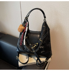 Detail of black suede tote bag with metal buckle strap and cute teddy bear charm