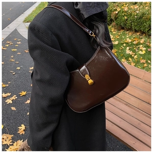 Detail of a dark brown patent leather shoulder bag with gold clasp and autumn foliage