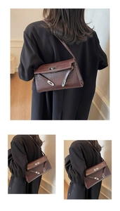 Detail view of dark coffee crocodile pattern texture and silver buckle on shoulder bag