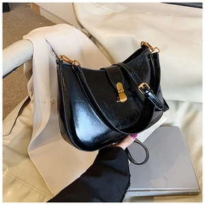Detail of black glossy leather underarm bag with iconic gold metal clasp and retro finish