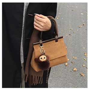 Détail du sac à main en daim marron avec anse en cuir et breloque singe en peluche en automne