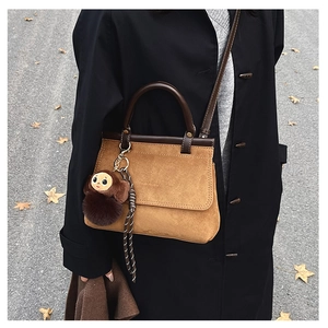 Sac à main en daim marron avec porte-clés singe sur fond de manteau noir